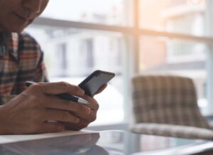 Insurance Savings - Close-up of a Man in a Flannel Shirt Using His Smart Phone and Laptop in a Cafe to Pay for Home Insurance